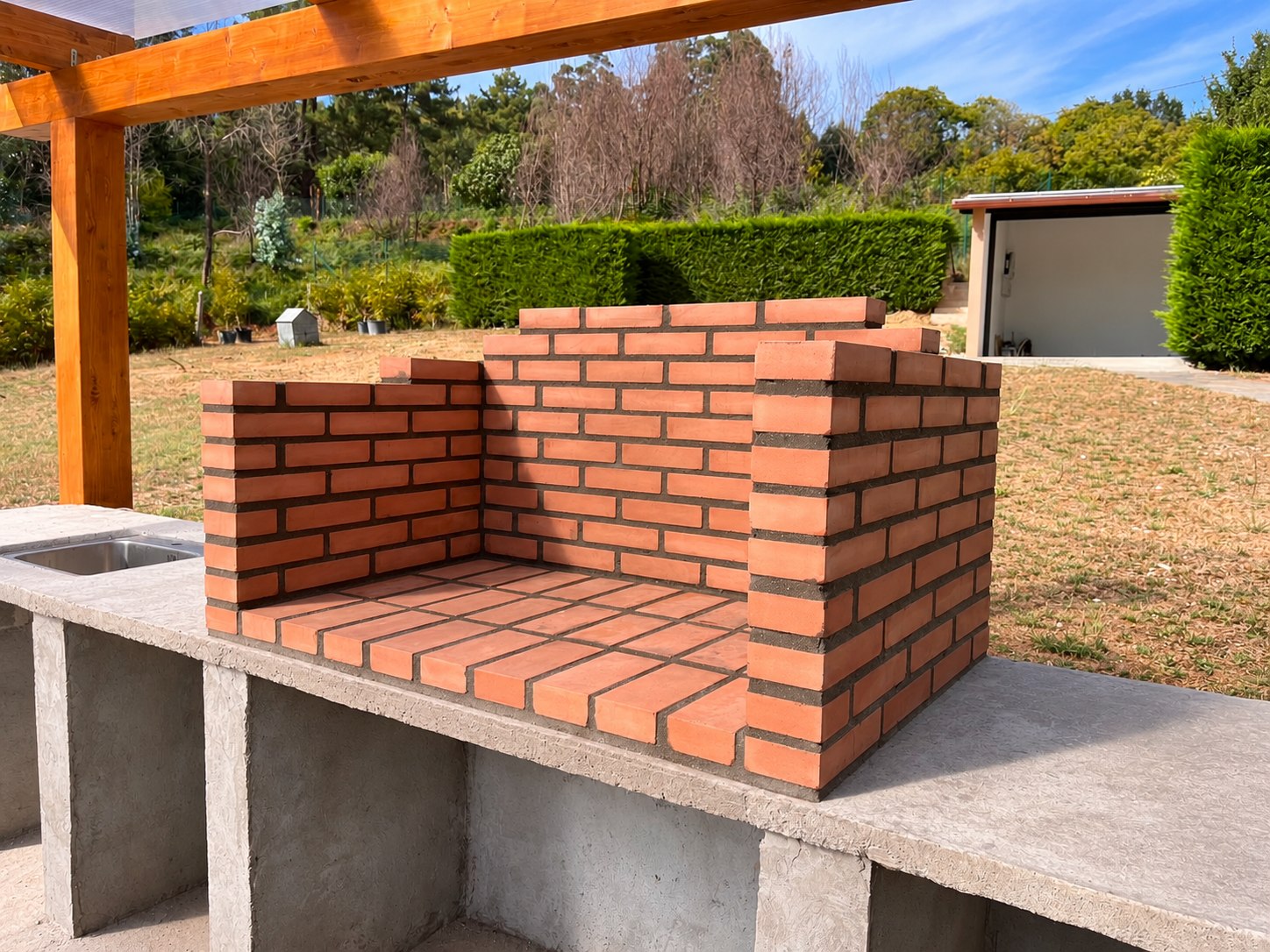 Barbacoa de ladrillo junto a fregadero bajo pérgola de madera; fotografía retocada