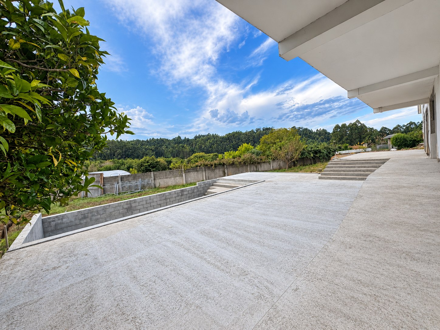 Terraza de hormigón, piscina en ejecución y escaleras junto a la vivienda; fotografía retocada