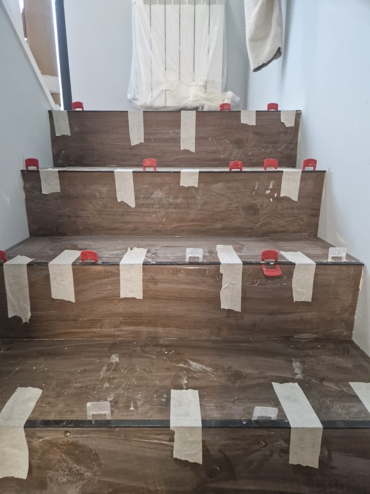 Escalera durante la colocación del revestimiento, con niveladores y cintas